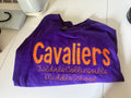 Purple shirt with 'Cavaliers' and school name printed on it, laid flat on a surface.